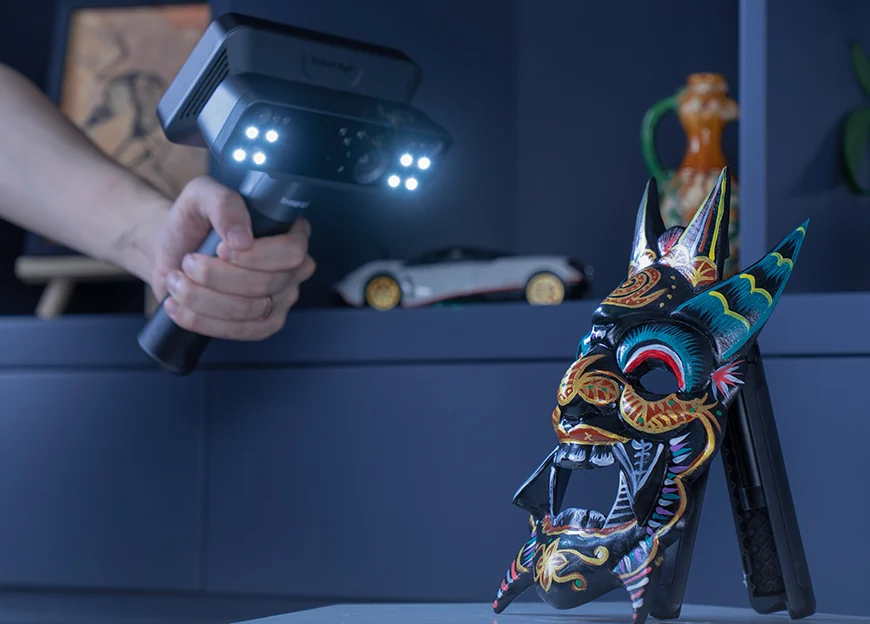 An EinScan Rigil scanner capturing a colourful decorative mask on a tabletop, with the scanner’s lights illuminating the object.
