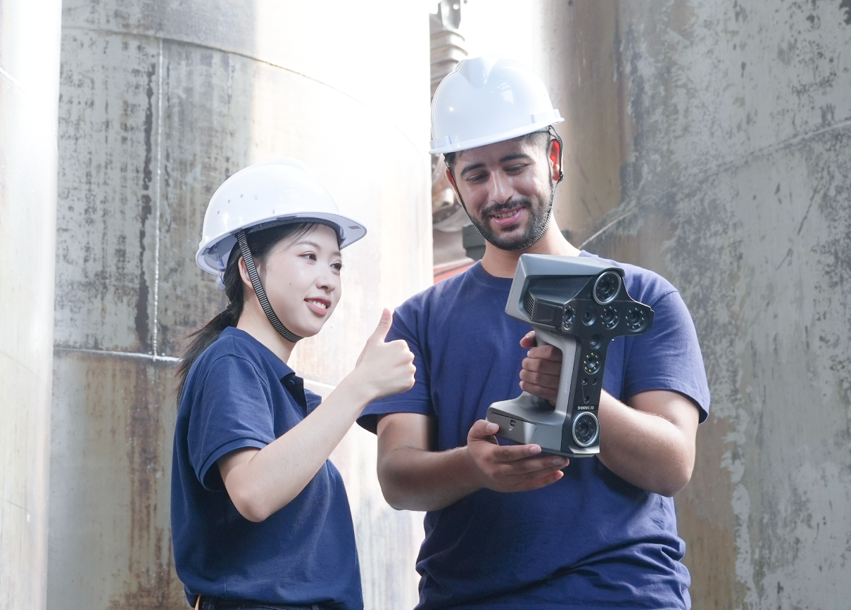 Two technicians wearing hard hats look at the EinScan Libre together at an industrial worksite.
