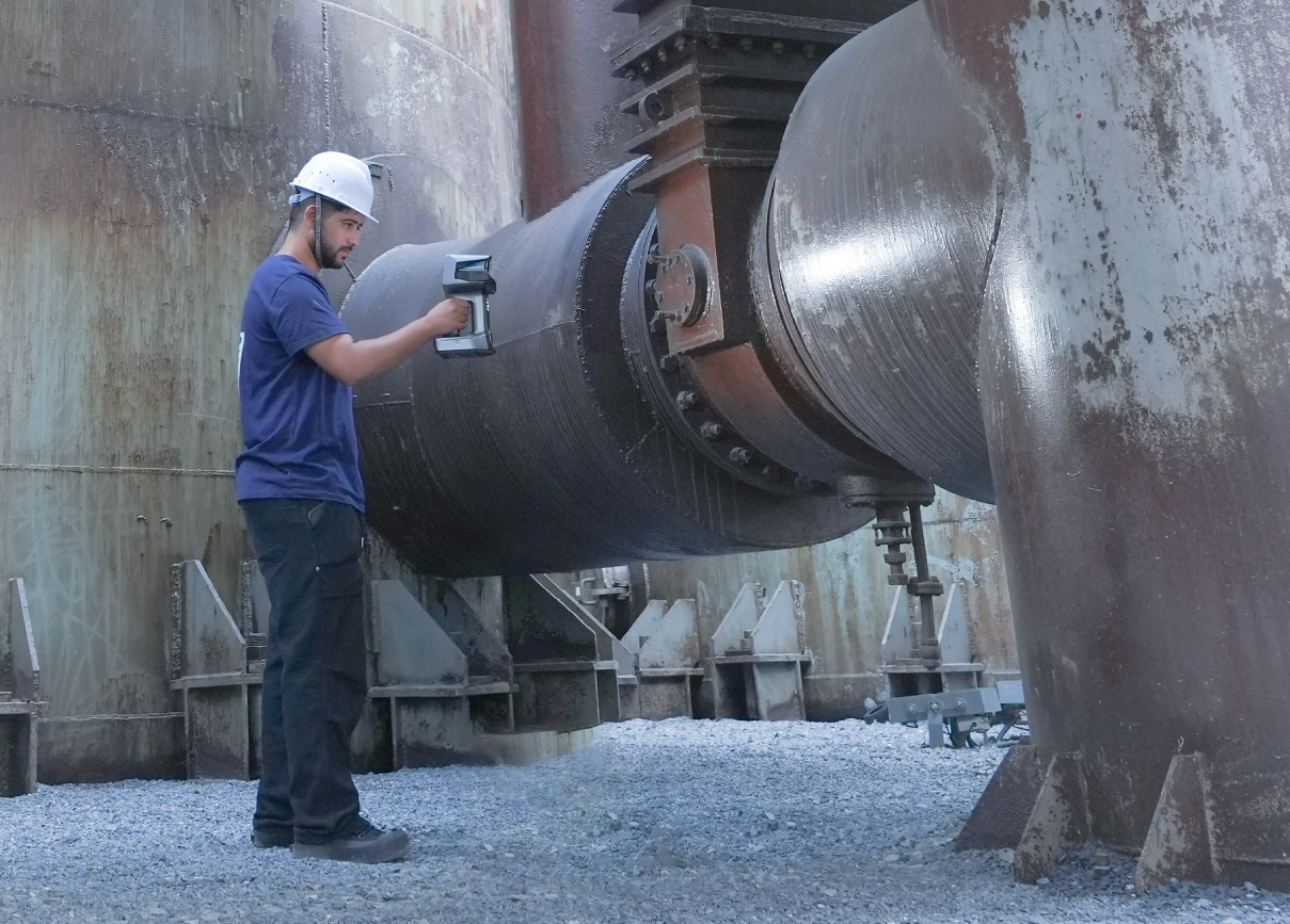 A technician in safety gear scans a large outdoor industrial pipe with the EinScan Libre.