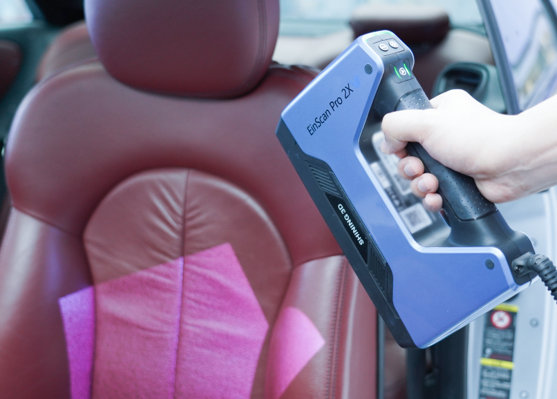 EinScan Pro 2X V2 handheld 3D scanner capturing the surface details of a car seat using markers.