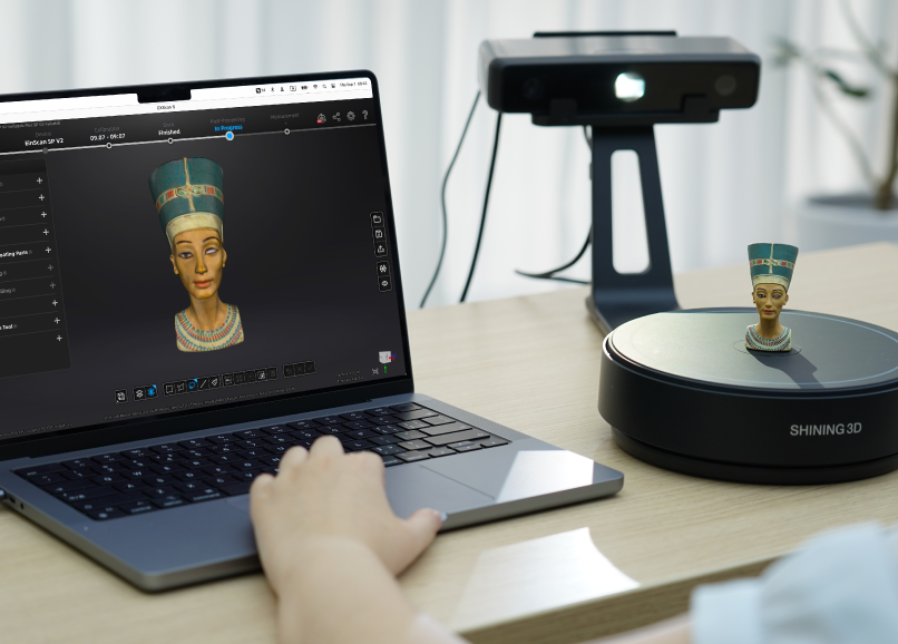 A user scanning a small Nefertiti bust with the EinScan SE V2, showing the coloured 3D model in the EXScan S software on a laptop while the turntable rotates the object.