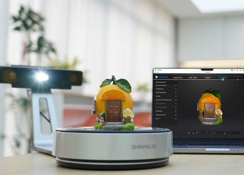 EinScan SP V2 scanning a small orange-themed model house on the turntable, with the 3D preview displayed on a laptop screen.