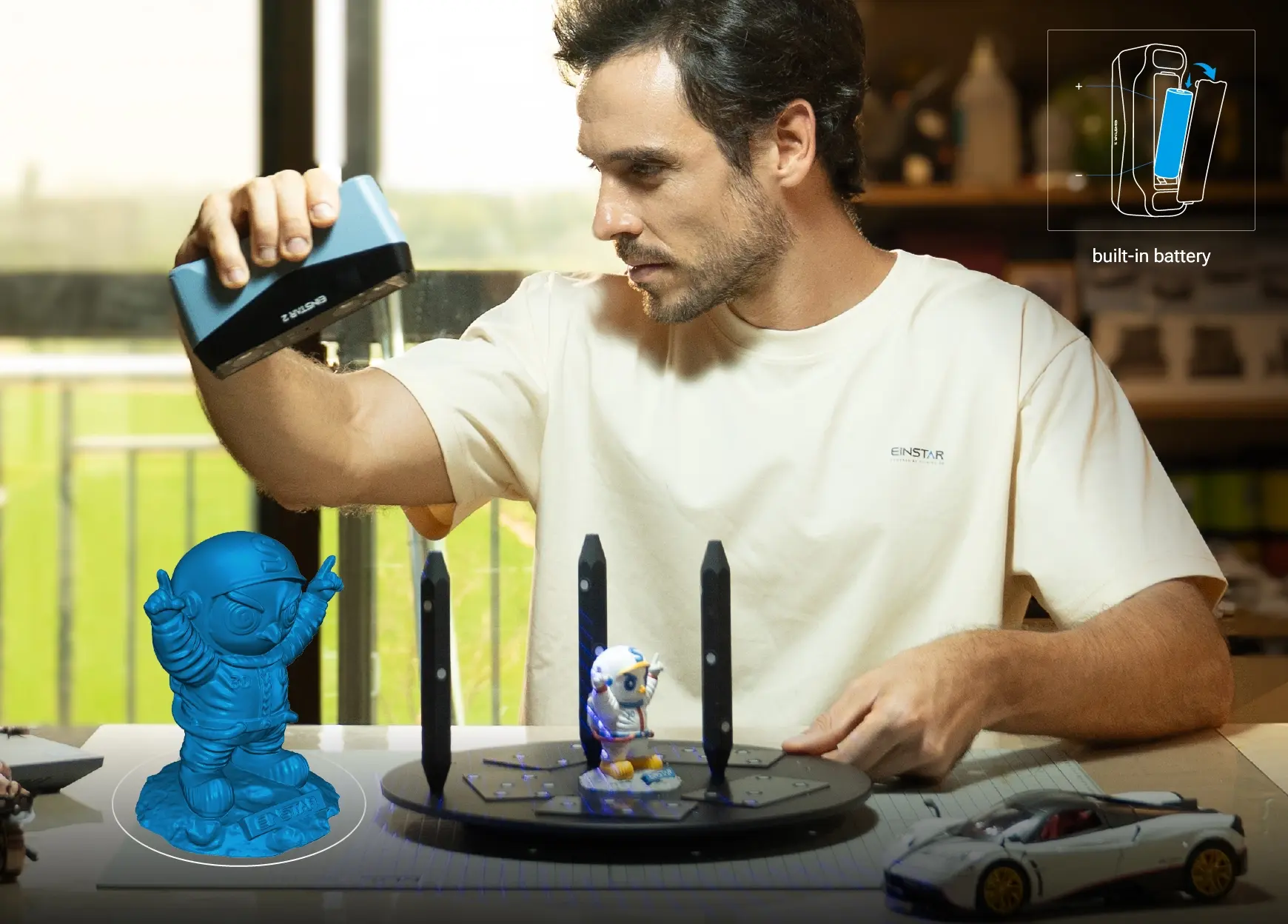 EINSTAR 2 scanning a small figurine on a turntable, with an overlay showing its swappable built-in battery for true wireless operation.
