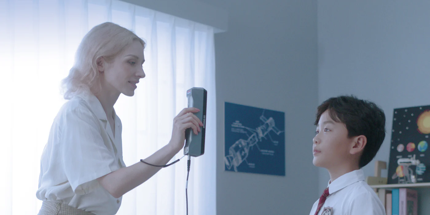 A person using an Einstar 3D scanner to capture a child’s face in a bright classroom setting.