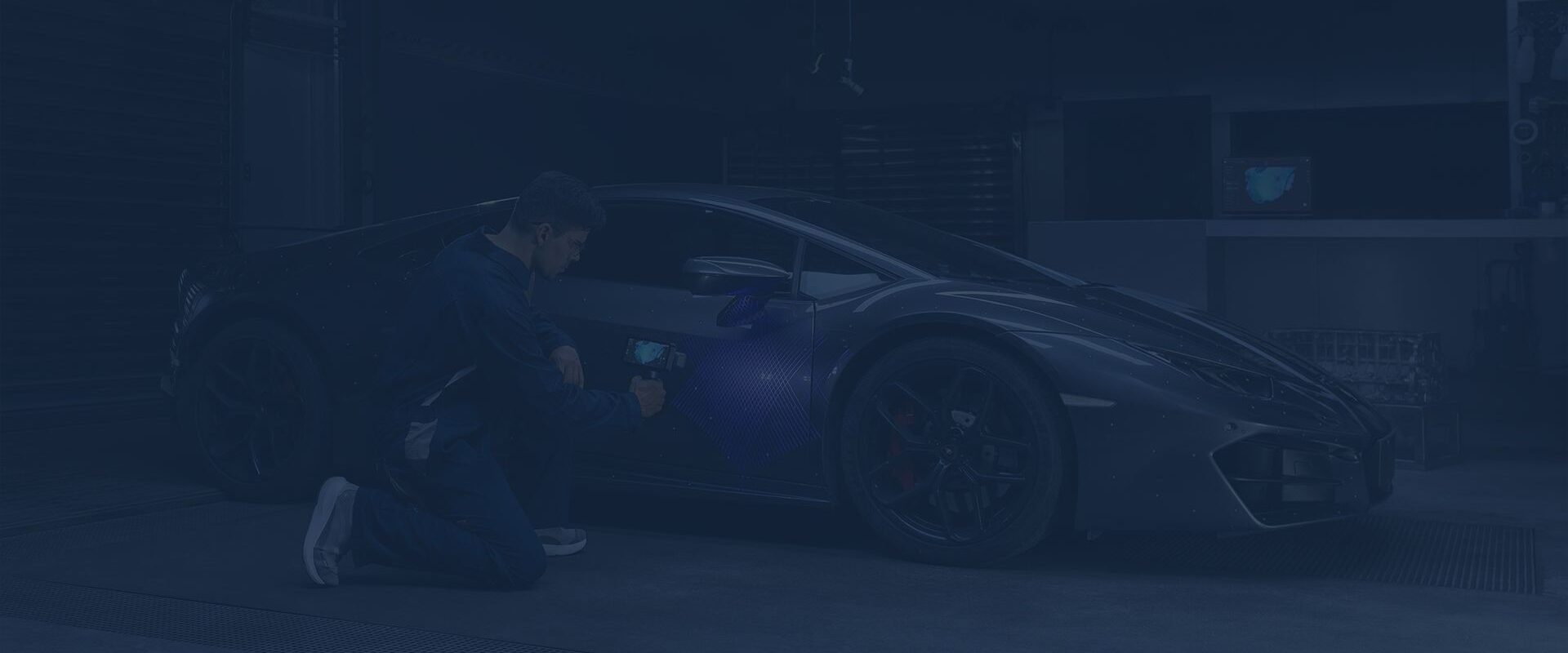 Technician using a handheld 3D scanner to capture the side of a sports car in an automotive workshop.